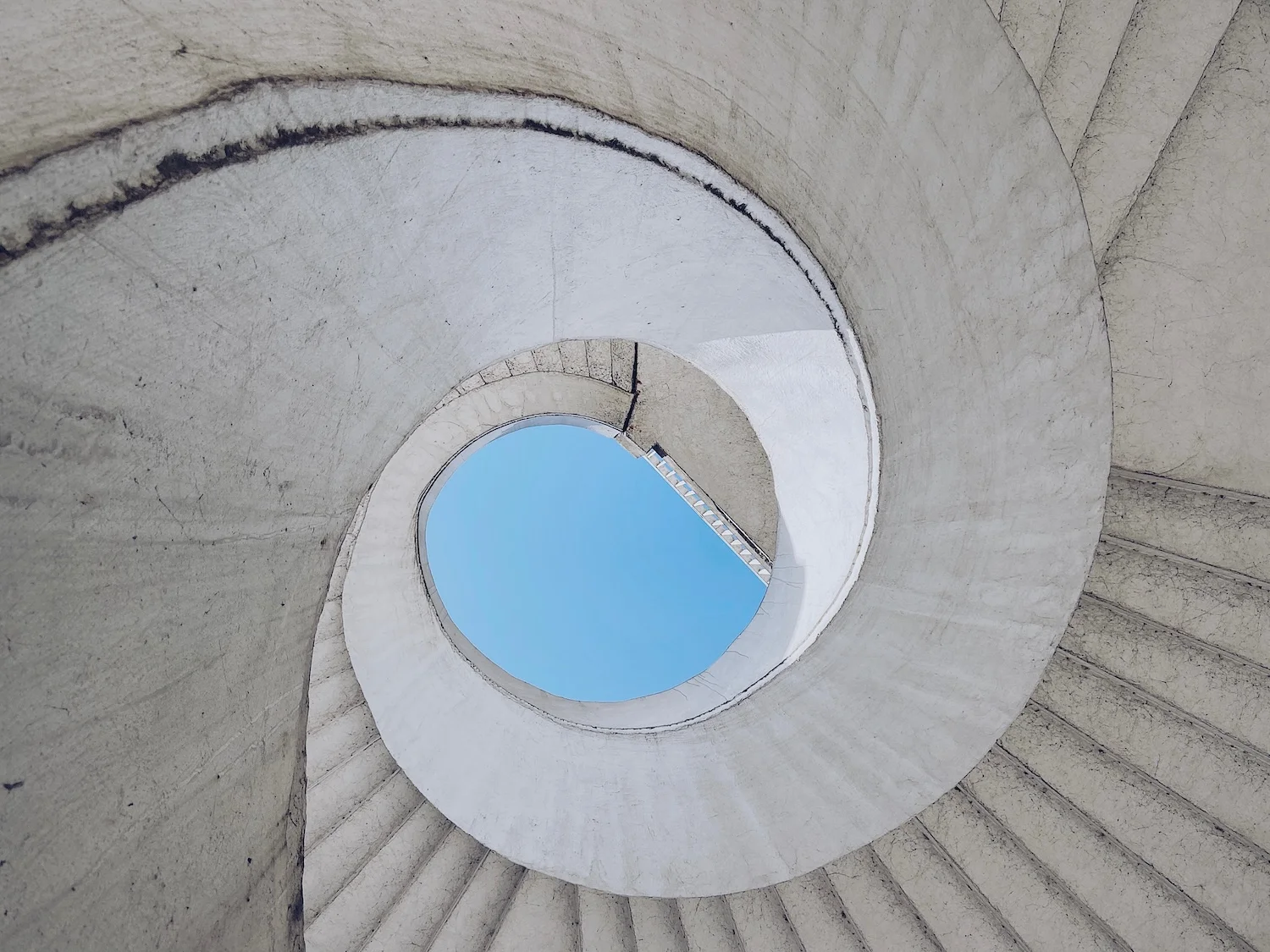 コンクリートの螺旋の中央に青空が見える建築