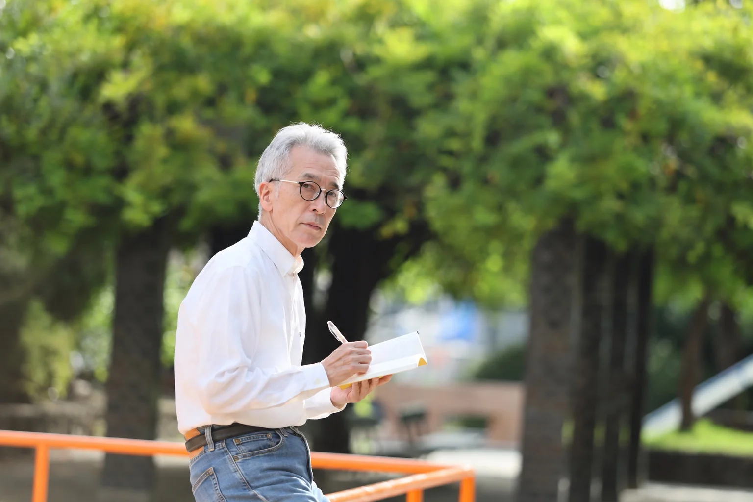 緑の中でノートとペンを持つタイヨシフミ